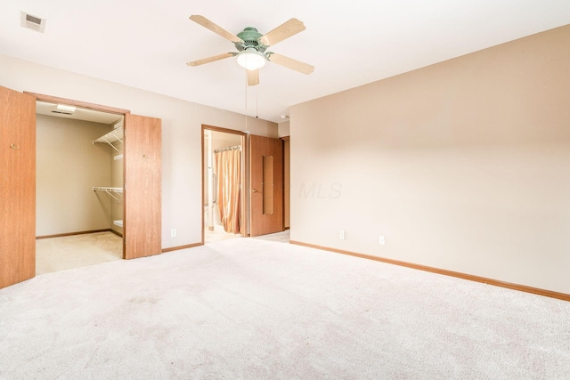 unfurnished bedroom with a spacious closet, ensuite bath, light carpet, a closet, and ceiling fan