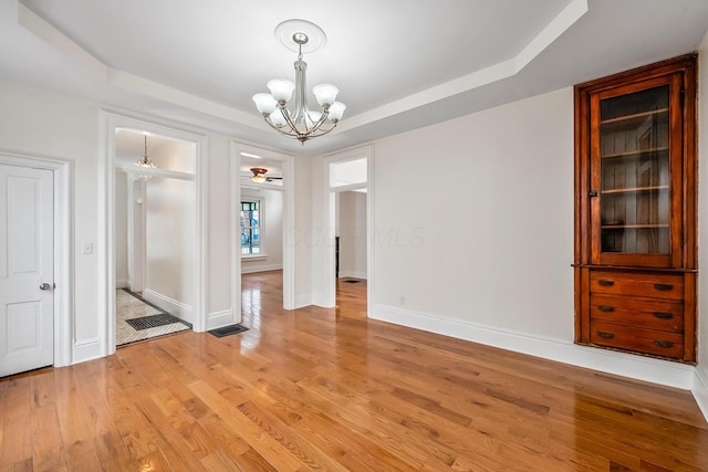 unfurnished dining area featuring light hardwood / wood-style floors, a raised ceiling, and a notable chandelier