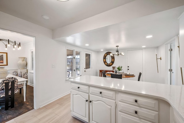 kitchen featuring light hardwood / wood-style flooring, hanging light fixtures, a notable chandelier, light stone countertops, and white cabinets