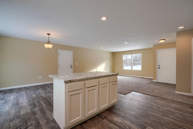 kitchen with a center island, white cabinetry, hanging light fixtures, light stone counters, and dark hardwood / wood-style floors