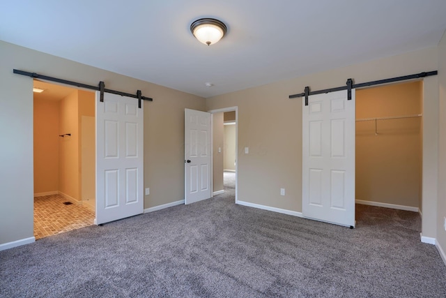 unfurnished bedroom with a walk in closet, a barn door, carpet floors, and a closet