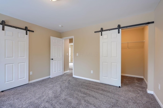 unfurnished bedroom with a spacious closet, a closet, a barn door, and carpet flooring