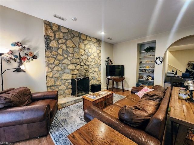 living room featuring built in shelves, wood-type flooring, and a fireplace