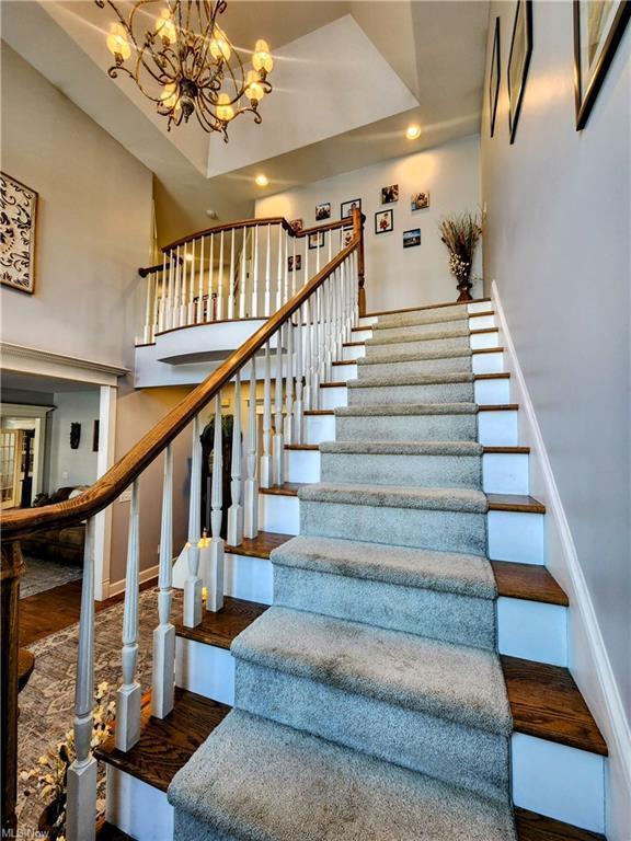 staircase with wood-type flooring, a towering ceiling, an inviting chandelier, and a tray ceiling