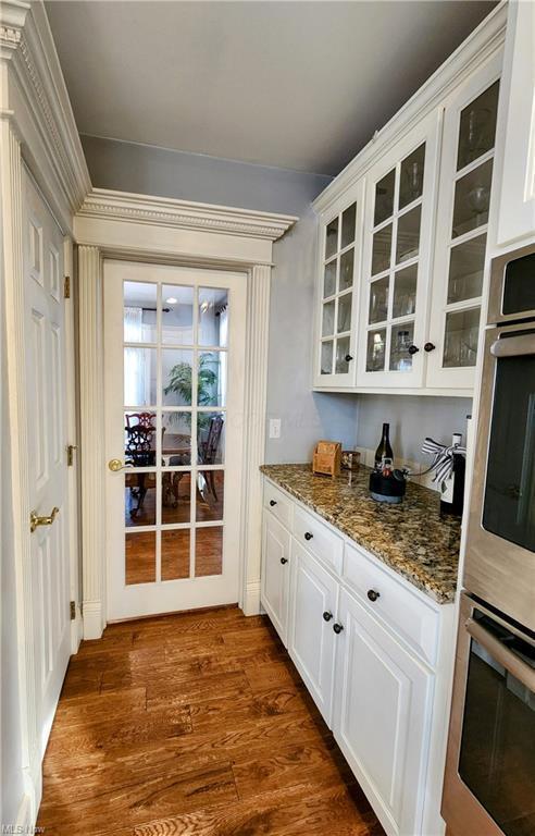 bar featuring white cabinetry, stainless steel double oven, dark hardwood / wood-style floors, and dark stone countertops