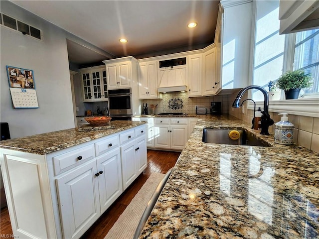 kitchen with white cabinetry, stainless steel double oven, light stone countertops, and sink