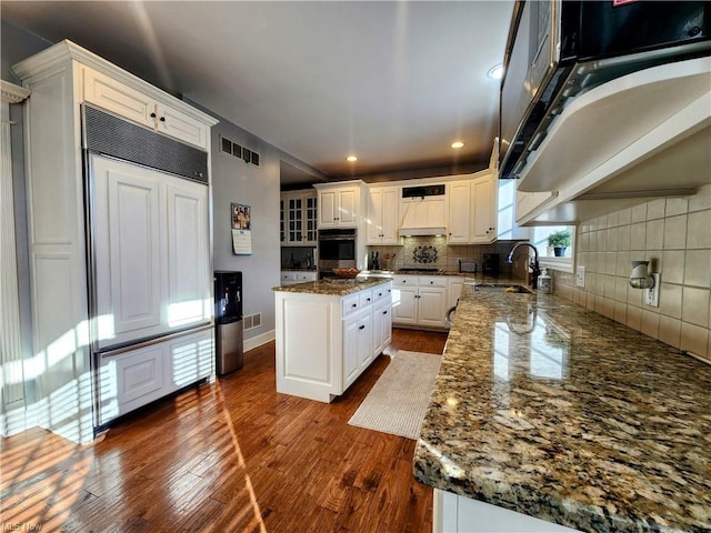 kitchen featuring a kitchen island, sink, white cabinets, dark stone counters, and dark wood-type flooring