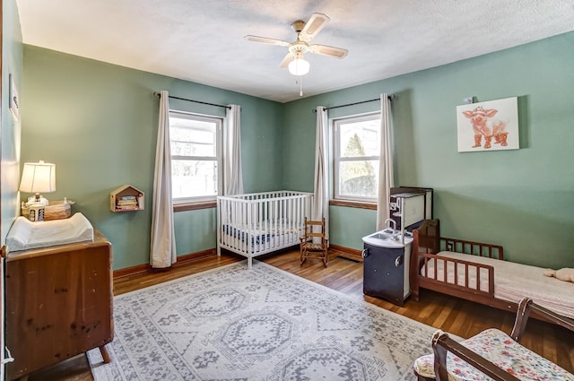 bedroom featuring ceiling fan, multiple windows, hardwood / wood-style floors, and a crib