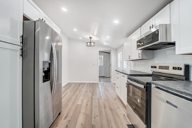 kitchen with vaulted ceiling, appliances with stainless steel finishes, white cabinets, backsplash, and light hardwood / wood-style floors