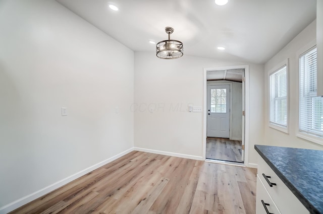 unfurnished dining area featuring vaulted ceiling and light hardwood / wood-style flooring