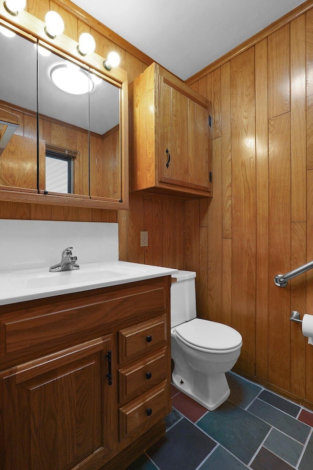 bathroom with toilet, vanity, and wood walls