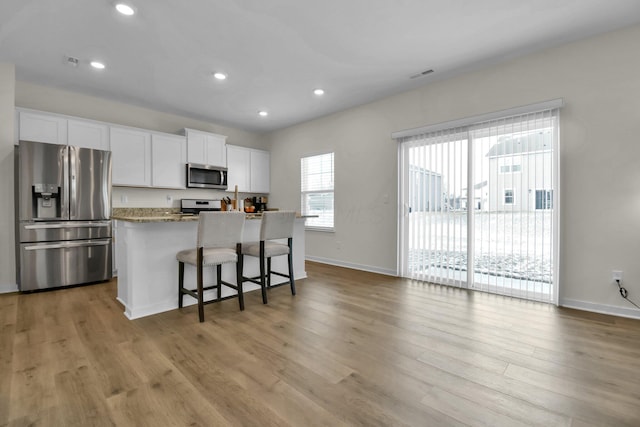 kitchen with white cabinets, a kitchen island, stainless steel appliances, light stone counters, and a breakfast bar