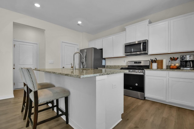 kitchen featuring white cabinets, stainless steel appliances, dark hardwood / wood-style floors, light stone counters, and a center island with sink