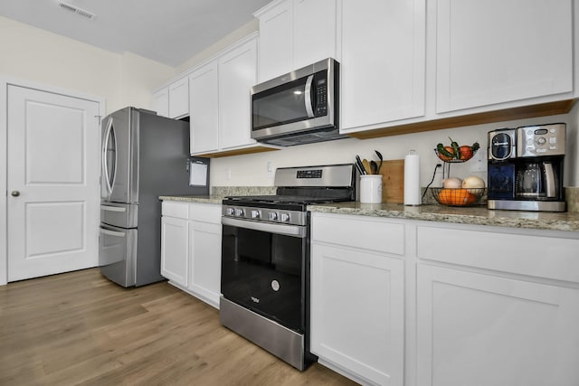 kitchen with light hardwood / wood-style floors, light stone countertops, white cabinets, and stainless steel appliances