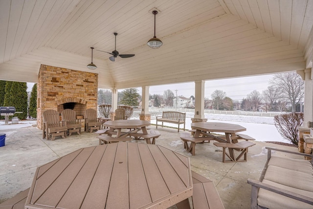 snow covered patio featuring ceiling fan, a gazebo, an outdoor stone fireplace, and area for grilling