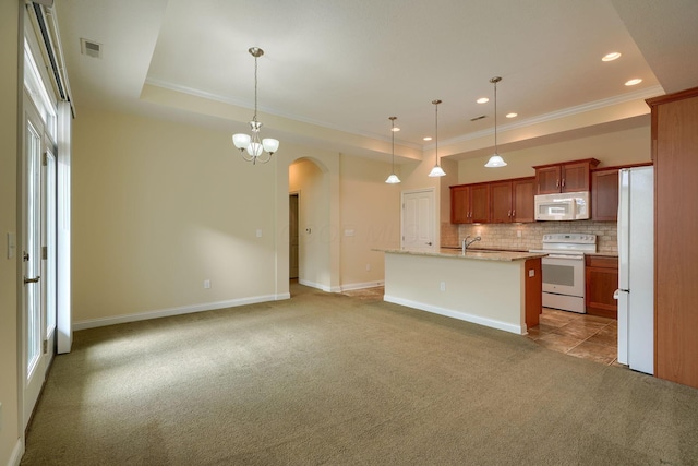 kitchen with decorative light fixtures, white appliances, a tray ceiling, and an island with sink