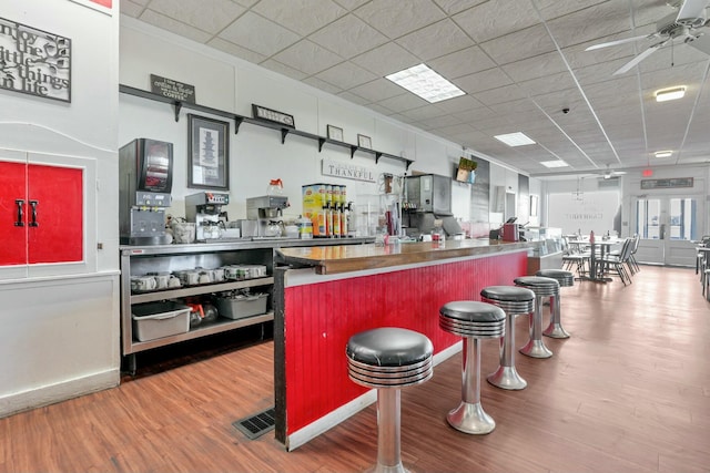 kitchen featuring a drop ceiling, ceiling fan, wood-type flooring, and a breakfast bar