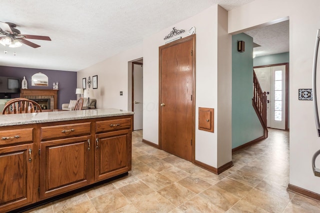 kitchen with ceiling fan, light stone counters, a fireplace, and a textured ceiling