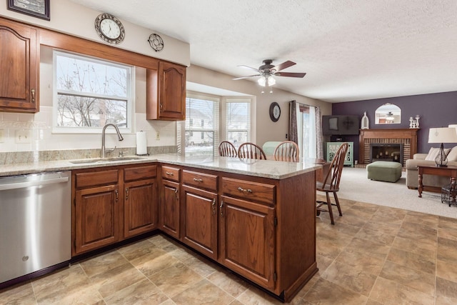 kitchen featuring a textured ceiling, a brick fireplace, stainless steel dishwasher, sink, and kitchen peninsula