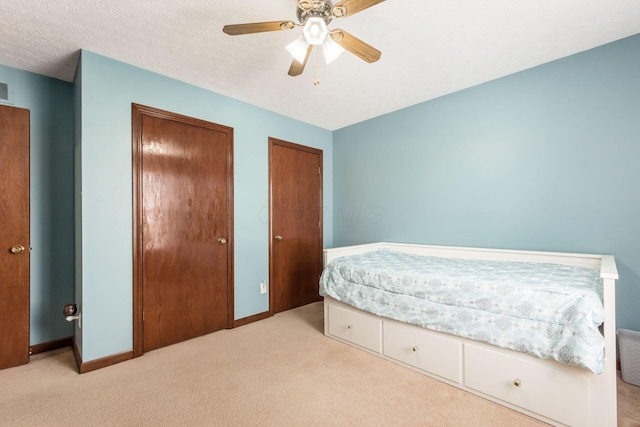 carpeted bedroom with multiple closets, a textured ceiling, and ceiling fan