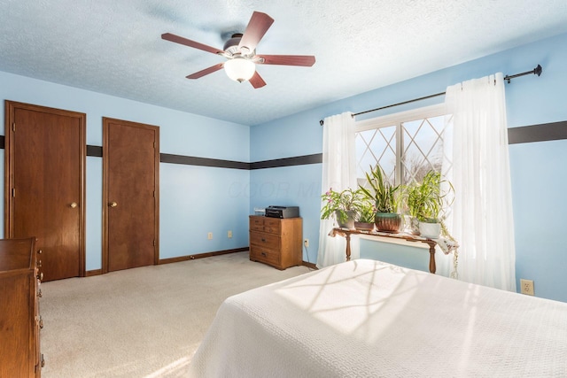 carpeted bedroom featuring multiple closets, a textured ceiling, and ceiling fan