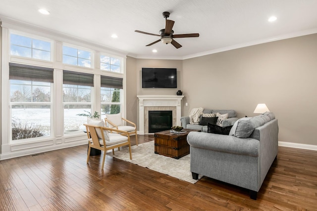 living room featuring a tiled fireplace, crown molding, ceiling fan, and dark hardwood / wood-style flooring