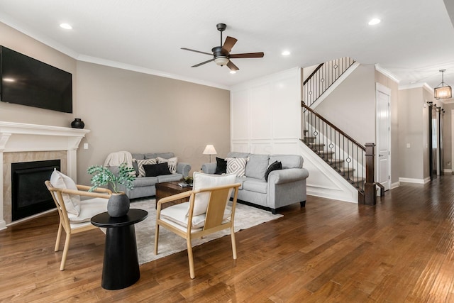 living room featuring hardwood / wood-style floors, crown molding, a tile fireplace, and ceiling fan