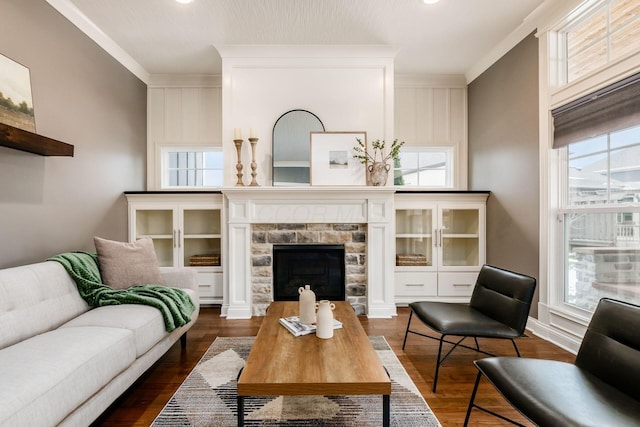 living room featuring dark wood-type flooring, ornamental molding, and a stone fireplace