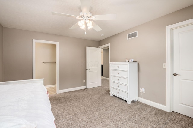 unfurnished bedroom featuring a spacious closet, light colored carpet, a closet, and ceiling fan