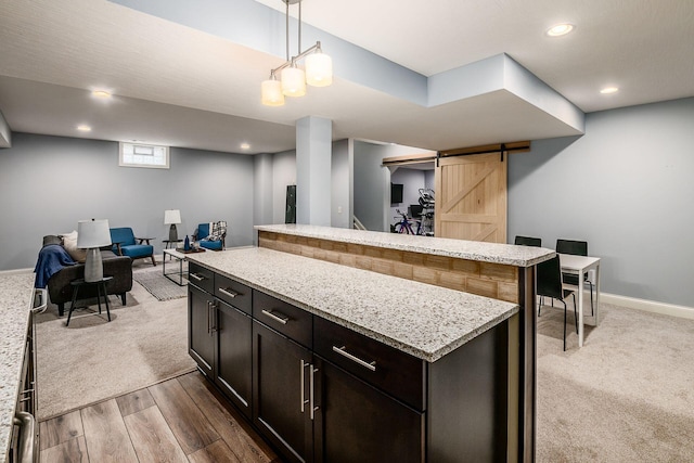 kitchen featuring hanging light fixtures, hardwood / wood-style floors, light stone counters, a kitchen island, and a barn door