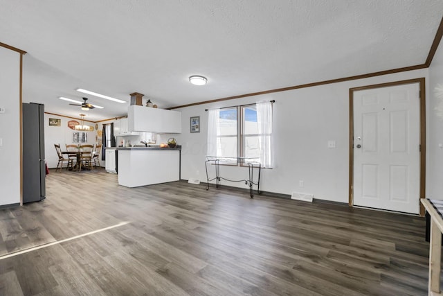 unfurnished living room with sink, crown molding, ceiling fan, dark hardwood / wood-style floors, and a textured ceiling