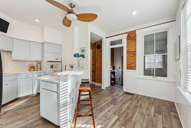 kitchen with tasteful backsplash, ceiling fan, oven, and light hardwood / wood-style floors