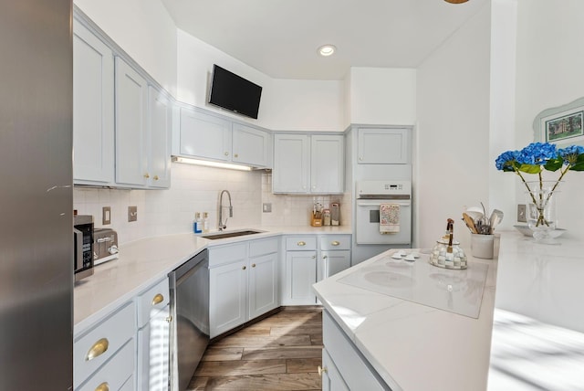 kitchen featuring sink, light wood-type flooring, stainless steel appliances, light stone countertops, and decorative backsplash