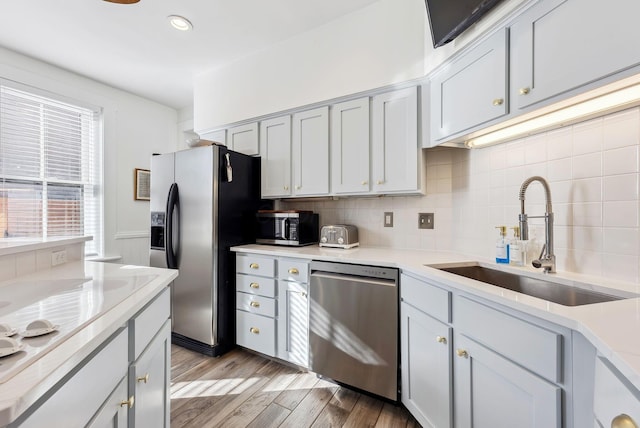 kitchen featuring sink, appliances with stainless steel finishes, gray cabinets, light hardwood / wood-style floors, and backsplash