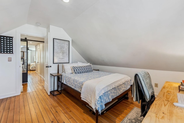 bedroom featuring vaulted ceiling, a barn door, and hardwood / wood-style floors