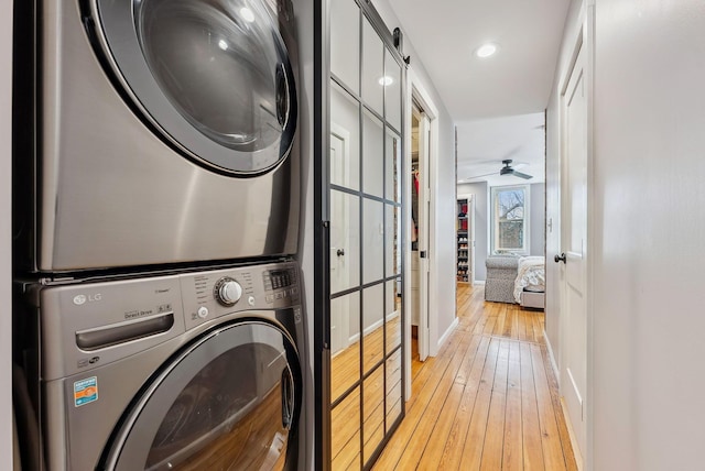 washroom with stacked washing maching and dryer, ceiling fan, and light hardwood / wood-style flooring