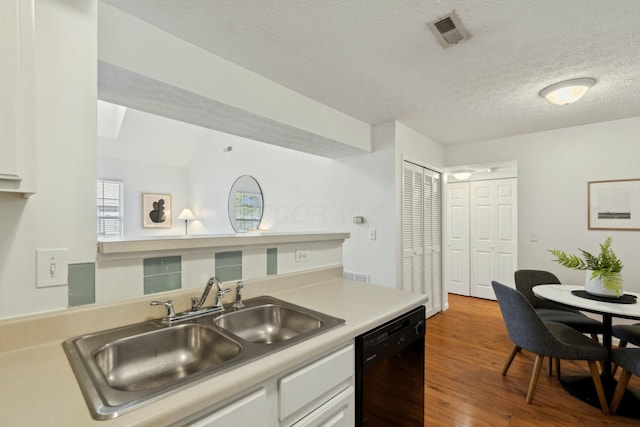 kitchen featuring black dishwasher, sink, white cabinets, hardwood / wood-style flooring, and a textured ceiling