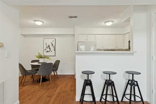 kitchen featuring hardwood / wood-style flooring, white cabinetry, a textured ceiling, kitchen peninsula, and white fridge