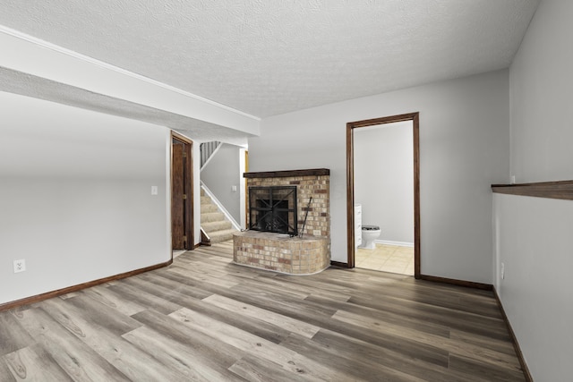 unfurnished living room featuring hardwood / wood-style floors, a textured ceiling, and a brick fireplace