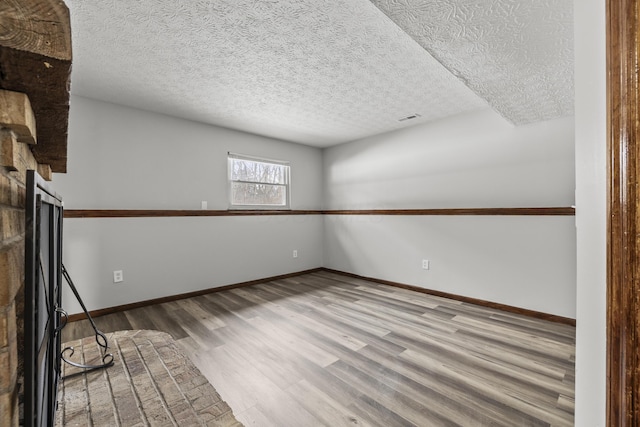 spare room with a brick fireplace, hardwood / wood-style floors, and a textured ceiling