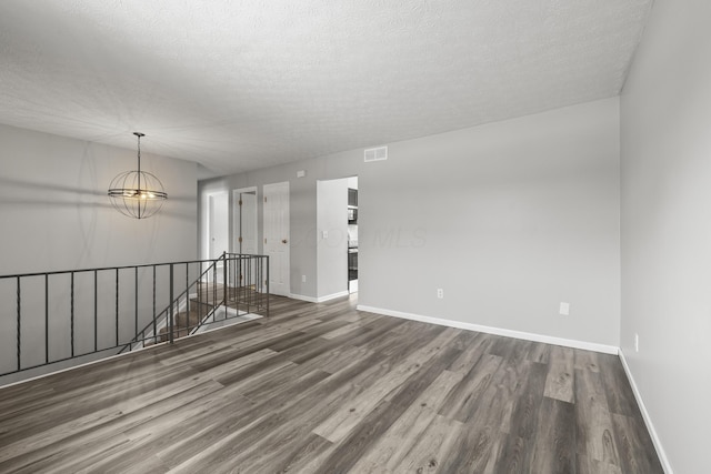 spare room featuring a chandelier, dark wood-type flooring, and a textured ceiling