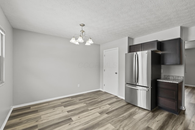 kitchen featuring pendant lighting, hardwood / wood-style floors, stainless steel fridge, a notable chandelier, and dark brown cabinets