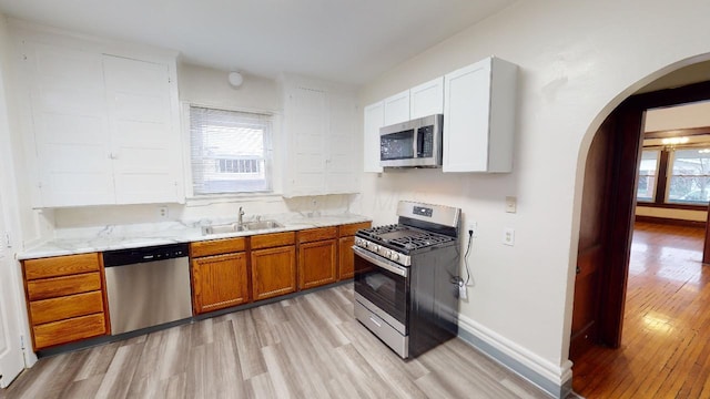 kitchen featuring sink, appliances with stainless steel finishes, light stone countertops, light hardwood / wood-style floors, and white cabinets