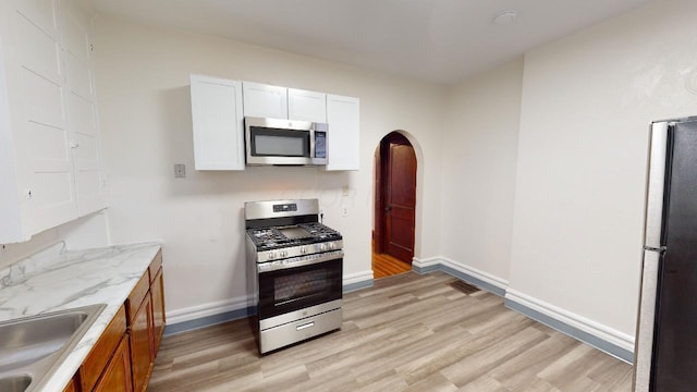 kitchen featuring appliances with stainless steel finishes, sink, white cabinets, light stone counters, and light wood-type flooring