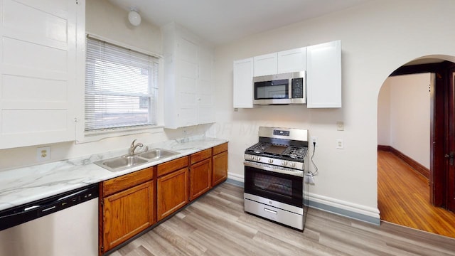 kitchen with stainless steel appliances, sink, light stone counters, and light wood-type flooring