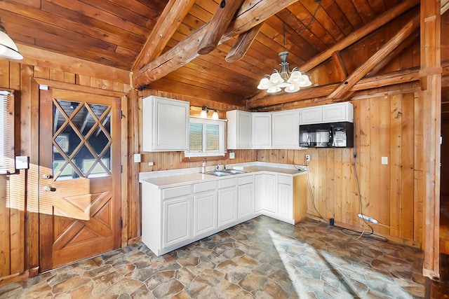 kitchen with hanging light fixtures, white cabinetry, vaulted ceiling with beams, a notable chandelier, and wooden walls