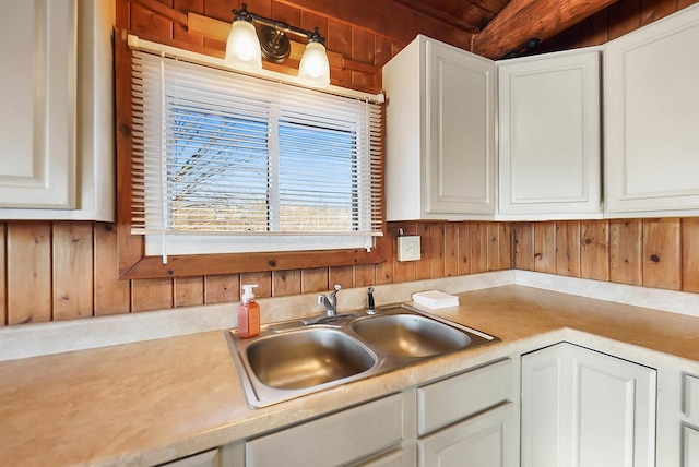 kitchen with sink, white cabinetry, and wooden walls