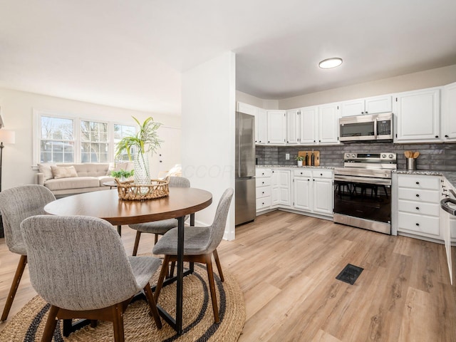 kitchen with light stone countertops, appliances with stainless steel finishes, white cabinetry, decorative backsplash, and light hardwood / wood-style flooring