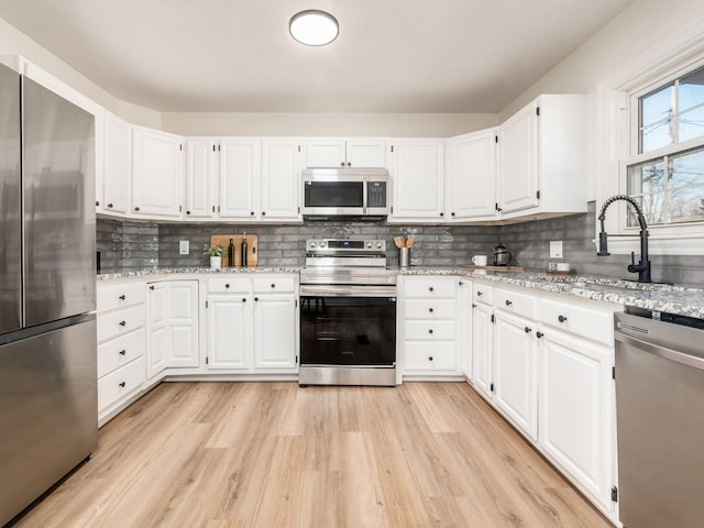 kitchen featuring backsplash, white cabinetry, light stone counters, and appliances with stainless steel finishes