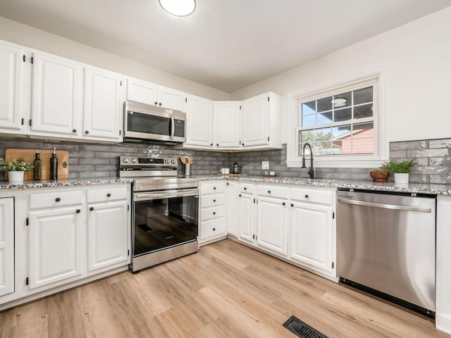 kitchen with light hardwood / wood-style floors, white cabinetry, and appliances with stainless steel finishes